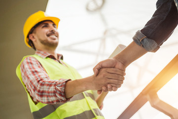 Engineer construction workers in protective helmets and vests are shaking hands while working in...