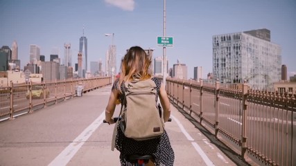 Back view female freelance worker with long flying hair enjoying weekend bike ride on Brooklyn Bridge, slow motion.