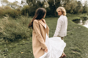 A beautiful couple in free clothes walks in the lawn near the lake on a sunny summer day