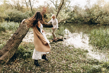 A beautiful couple in the boo style embraces sitting on a branch over the lake