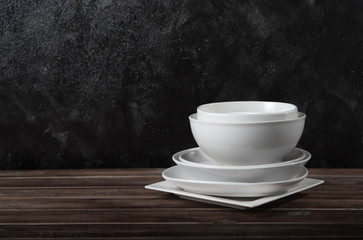 Stack of white ceramic dishware on wood against black cement wall