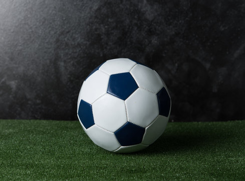 Soccer ball on green grass against black cement wall