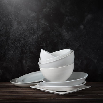 Stack of white ceramic dishware on wood against black cement wall