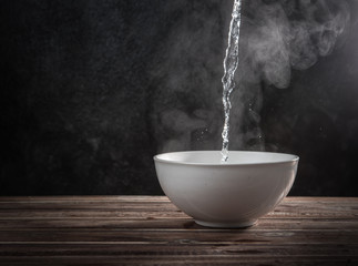 Pouring hot water into into a ceramic bowl against black cement wall