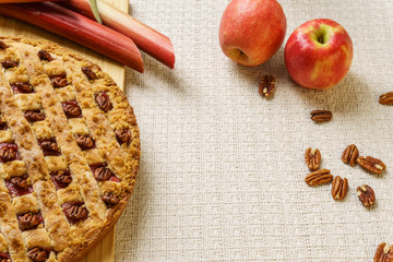 Whole apple and rhubarb pie with pecan on a black tray on a table.