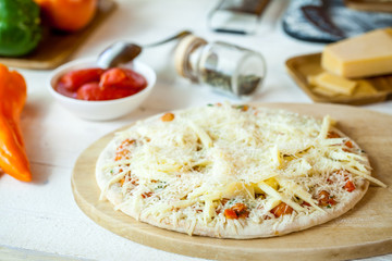closeup raw fresh homemade traditional italian cheese pizza ready to cook on wooden cooking table with ingredients. wallpaper for pizzeria and food concept