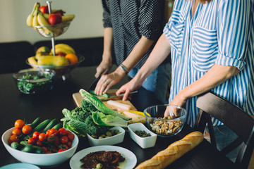 Two women cutting fresh vegetables for green veggie salad, healthy food cooking