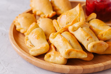 Two types of empanadas on a wooden plate with ketchup. White stone background.