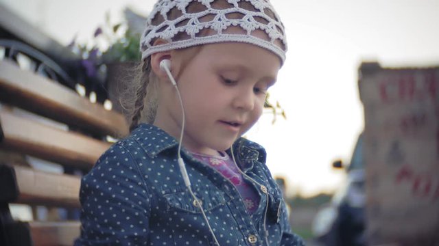 Little stylish beautiful gerl, on city streets listening to music in l headphones.