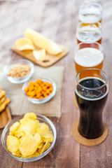 glasses of light and dark beer with assorted snacks on a wooden
