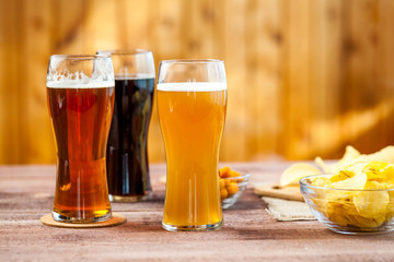 glasses of light and dark beer with assorted snacks on a wooden table background. bachelor party, pub, bar or degustation concept