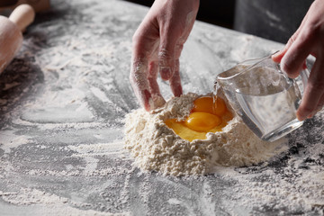 women's hands pours water into the flour on the kitchen table. Preparation of dough for baking