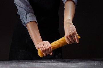 chef in an apron breaks a handful of raw Italian spaghetti