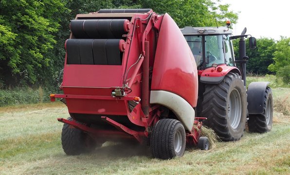 Hay baler machine pulled by a red tractor on a freshly cut field