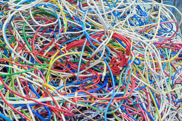 The bunch of electric wires of different colors are very much intertwined. On tangled wires is wire-end ferrules and markings. Chaos, confusion, tangle. Abstract background.