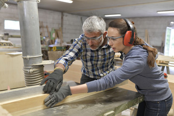 Carpenter teaching apprentice how to cut wood