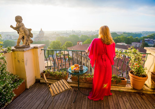 Woman standing on balcony and overlooking city in morning