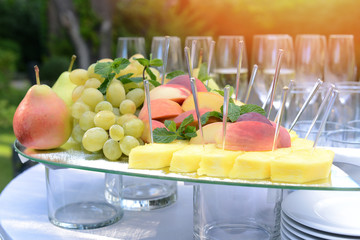 fresh fruits, pears grapes slices of peaches and pineapples on a glass tray at banquet on summer sunny day