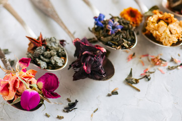 Assortment of dry green herbal and flower tea in a spoons on a white stone background.