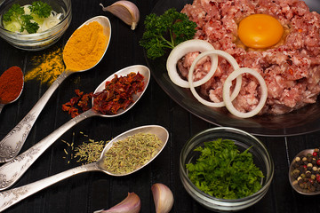 Minced meat. Ground meat with ingredients for cooking on a black background.