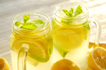 Two mason jar glasses of homemade refreshing lemonade, slices of organic ripe lemon, whole and halved, mint leaves, juicer, muddler, squeezer on a rustic white wooden background. Close up, top view.