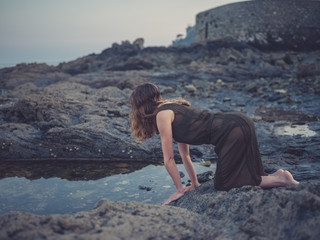 Young woman by rock pool on coast at sunset