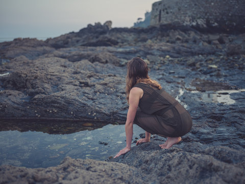 Young woman by rock pool on coast at sunset