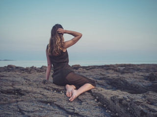 Fototapeta na wymiar Young woman sitting on coast at sunset