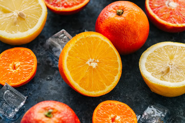 Mix of fresh ripe citrus fruits as blood oranges, mandarines, lemons  with ice cubes on a blue stone background. Top view.