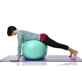 Female fitness instructor holds legs in gym and workout exercises for abdominals with green sport ball over white