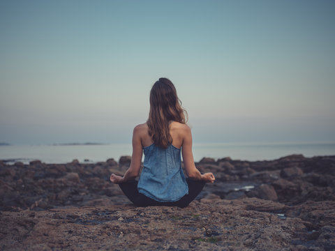 Young woman meditating on coast at sunset