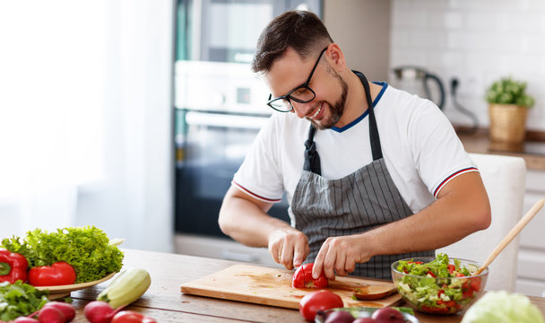 happy  man preparing vegetable salad in kitchen