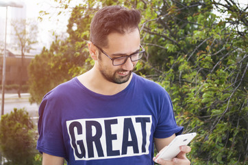 Attractive young smiling man using phone in a public park