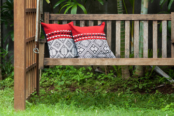 Fragment of wooden swing in the green garden with pillows