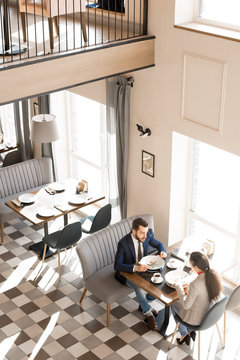 Directly above view of calm confident business colleagues sitting at table and enjoying tasty food while having lunch break, they visiting cozy restaurant