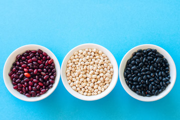 Tree types of dried beans in a white bowls on a light blue background. Top view. Healthy eating concept.