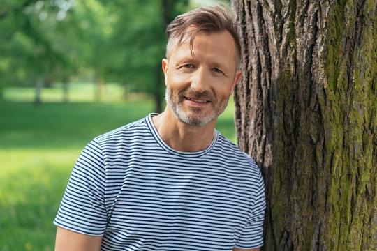 Casual middle-aged man leaning on a tree trunk