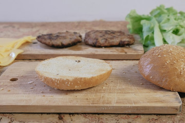 Products for preparation of burgers: buns, cutlets, cheese, salad, on the table. Side view.