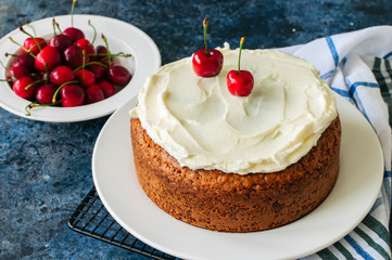 Homemade sour cream cake with cream cheese frosting decorated with fresh ripe cherries.