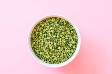 Dry uncooked green peas in a white bowl on a light pink background. Top view and copy space.