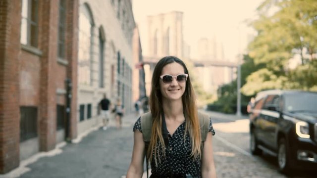 Camera follows happy excited European tourist girl with backpack and camera in sunglasses smiling, turning around 4K.