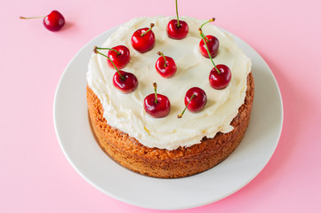 Homemade sour cream cake with cream cheese frosting decorated with fresh ripe cherries on a light pink background. Close up.