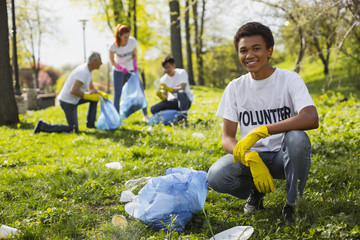 Volunteering problem. Cheerful male volunteer smiling to camera while collecting litter