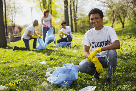 Volunteering problem. Cheerful male volunteer smiling to camera while collecting litter
