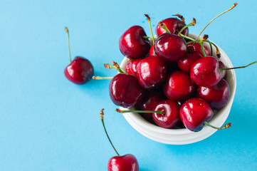 Fototapeta na wymiar Heap of fresh ripe red cherries in a white bowl on a light blue background. Top view and copy space. Organic food concept.