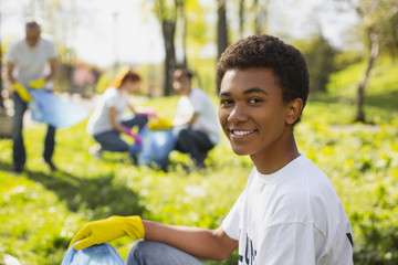 Rehabilitation of nature. Afro american male volunteer gazing at camera while collecting litter