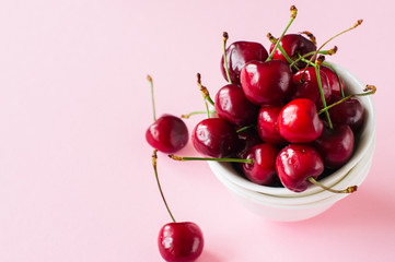 Obraz na płótnie Canvas Heap of fresh ripe red cherries in a white bowl on a light pink background. Top view and copy space. Organic food concept.