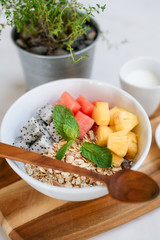 Bowl of Asian heathy breakfast from top view includes grain dragon fruit, pine apple, papaya and cup of milk and honey