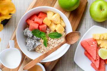 Bowl of Asian heathy breakfast from top view includes grain dragon fruit, pine apple, papaya and cup of milk and honey