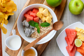 Bowl of Asian heathy breakfast from top view includes grain dragon fruit, pine apple, papaya and cup of milk and honey